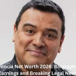 Carlos Mencia smiling in a close-up portrait, wearing a black leather jacket, featured in an article about Carlos Mencia Net Worth, career earnings, biography, and legal news.