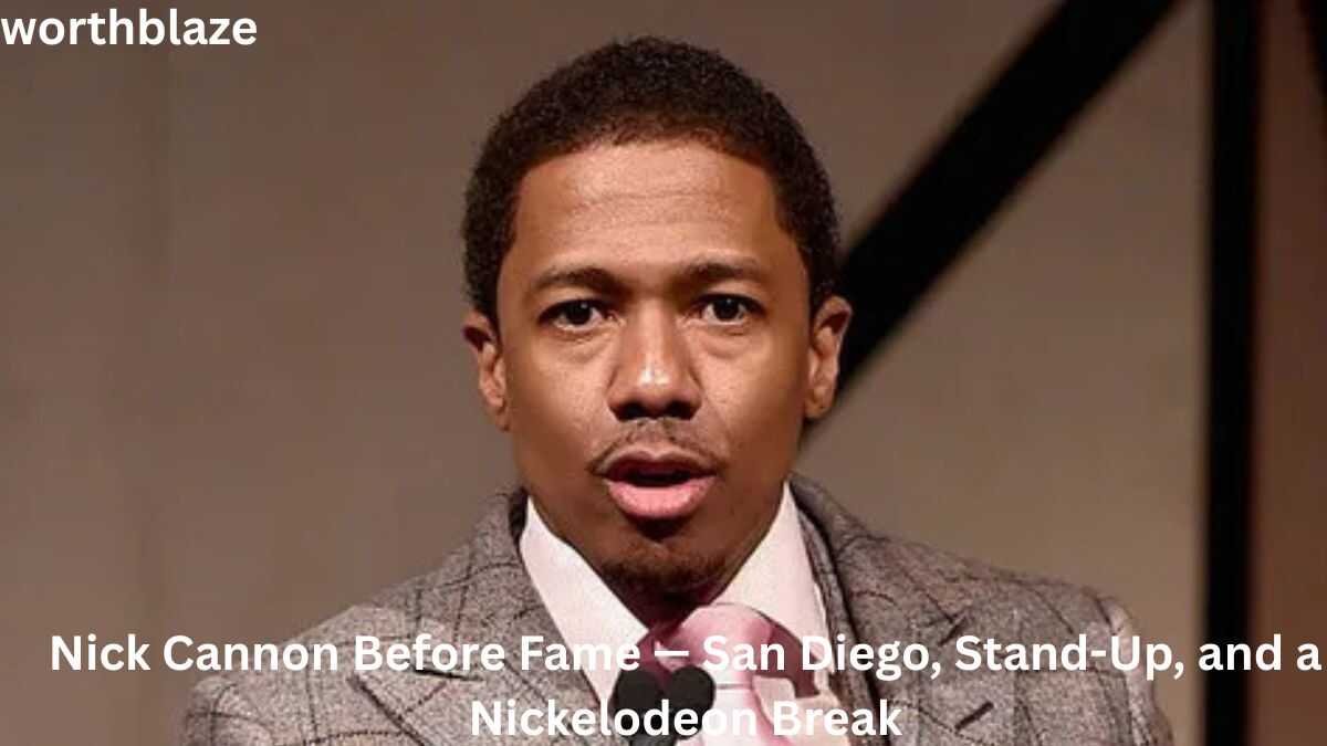 Nick Cannon speaking at an event in a gray suit and pink tie, highlighting his career journey and success related to Nick Cannon Net Worth.