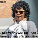 Lauryn Hill wearing sunglasses and a large white bow blouse, featured in an article about Lauryn Hill Net Worth 2026 and her estimated $500,000 fortune.