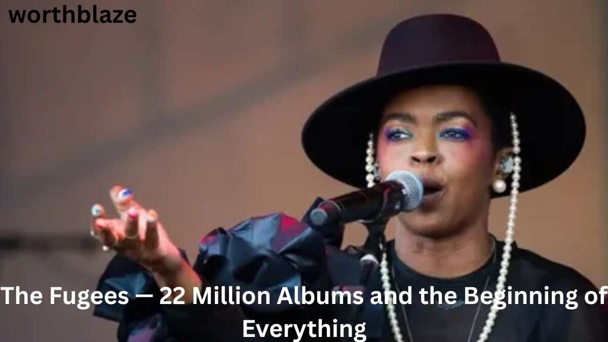 Lauryn Hill performs on stage with a microphone, wearing a black hat and pearl earrings during a live concert. Featured in an article about Lauryn Hill Net Worth 2026 and the success of The Fugees.